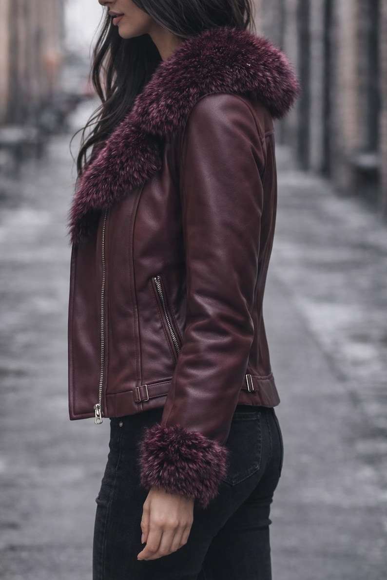 May include: Burgundy leather jacket with a faux fur collar and cuffs. The jacket features a zipper closure and a tailored fit. The model is wearing black jeans. The jacket is a stylish outerwear option.