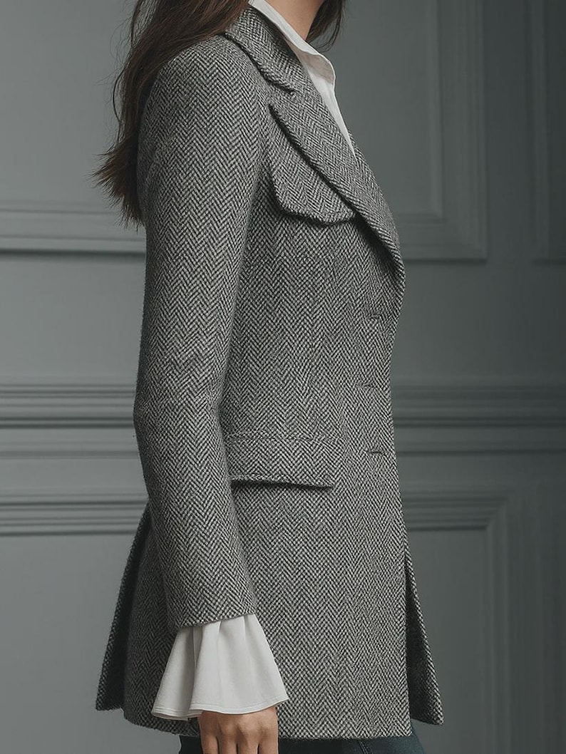 Puede incluir: Un blazer gris con estampado de espiga, solapa con muescas y cierre de un solo bot&oacute;n. El blazer tiene un bolsillo con solapa y un dobladillo acampanado. Las mangas son largas y se ven los pu&ntilde;os de una camisa blanca. Una prenda cl&aacute;sica y a medida.
