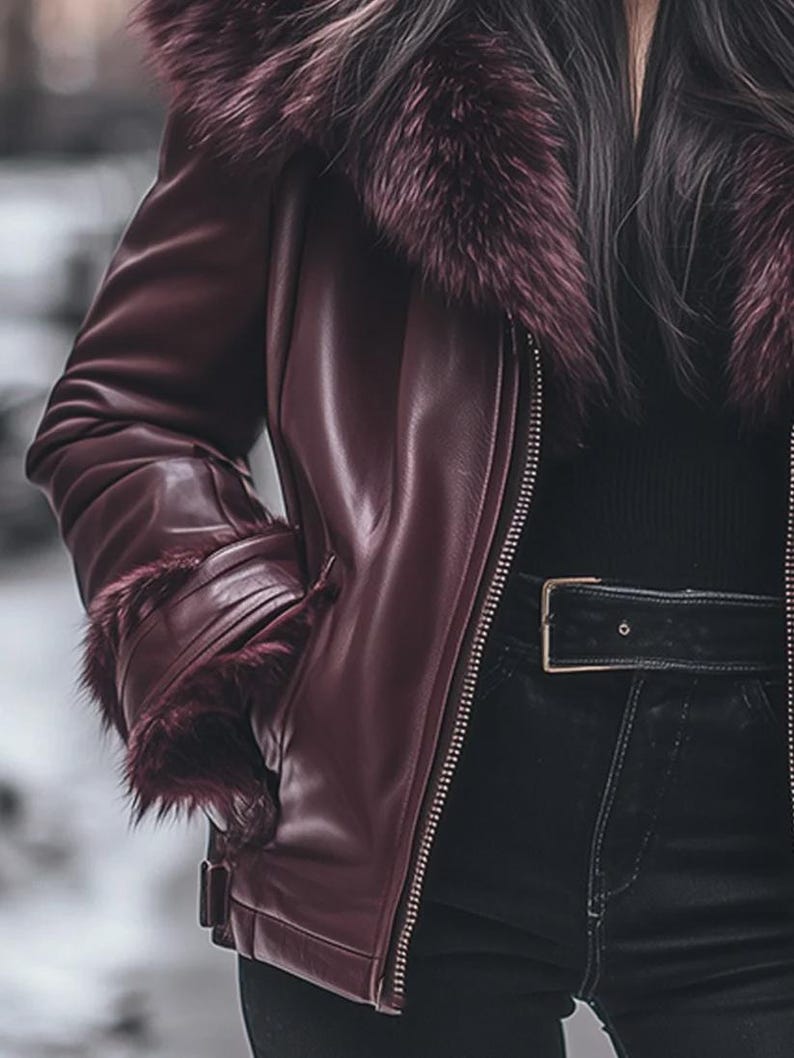 May include: A burgundy leather jacket with a faux fur collar and cuffs. The jacket features a zipper closure and a black belt with a gold buckle. The model is wearing black pants.