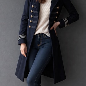Könnte beinhalten: Marineblauer Mantel im Militärstil mit goldenen Knöpfen und dekorativen Nähten. Der Mantel hat ein doppelreihiges Design und wird mit einem weißen Pullover und einer blauen Jeans getragen. Die Ärmel haben dekorative Streifen.