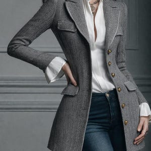 Puede incluir: Una blazer gris con estampado de espiga y botones dorados, combinada con una camisa blanca con cuello y vaqueros azul oscuro. La blazer tiene un corte entallado y presenta dos bolsillos delanteros. Las mangas tienen pu&ntilde;os blancos.