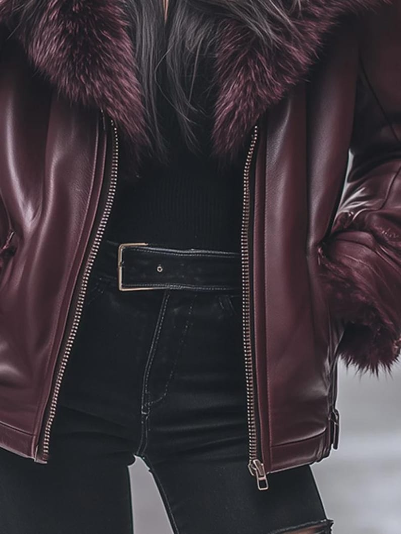 May include: A burgundy leather jacket with a faux fur collar and cuffs. The jacket features a zipper closure and a black belt. The model is wearing black jeans.