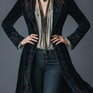 Puede incluir: Abrigo largo de terciopelo azul oscuro con intrincados bordados florales en los bordes y las mangas. Se combina con una blusa color crema, vaqueros azules y collares superpuestos. El estilo es bohemio.