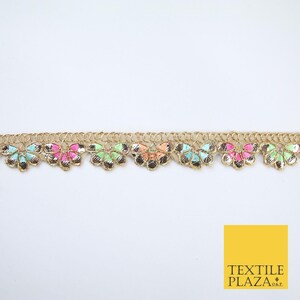 May include: A decorative trim with a repeating pattern of colourful, fan-shaped embellishments. The trim has a gold metallic base with turquoise, pink, orange, and green accents. The Textile Plaza logo is in the bottom right corner.