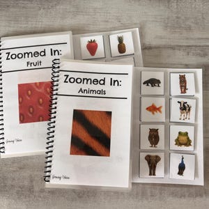 May include: Two spiral-bound educational booklets titled Zoomed In: Fruit and Zoomed In: Animals. The covers feature close-up textures of a strawberry and tiger fur. Each booklet includes white cards with full images of fruits and animals.