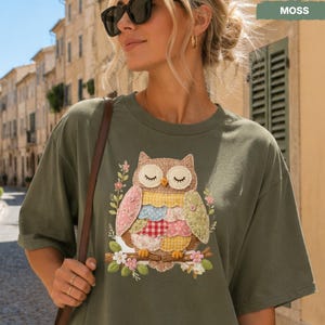 May include: Olive green t-shirt featuring a colorful owl graphic. The owl design includes various fabric patterns and floral accents. The word "MOSS" is printed on the top right corner of the image.