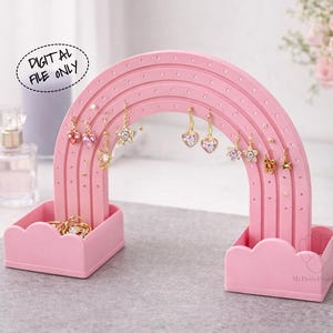 Könnte beinhalten: Ein rosa Regenbogen-Ohrringhalter mit mehreren Löchern zur Präsentation von Ohrringen. Der Halter hat zwei wolkenförmige Sockel und eine Reihe von gebogenen Bögen. Mehrere Ohrringpaare sind auf dem Halter ausgestellt. Der Text "DIGITAL FILE ONLY" befindet sich in einer Sprechblase.