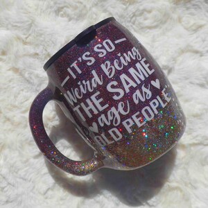 May include: A glitter-covered coffee mug with a black rim and handle. The mug is a gradient of purple, gold, and green glitter. White text on the mug reads, "It's so weird being the SAME age as OLD PEOPLE."
