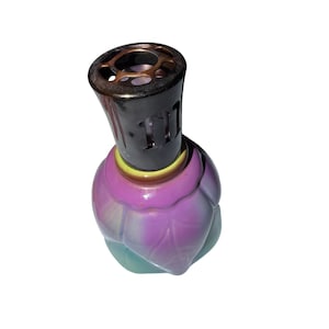 May include: A fragrance lamp with a rounded glass body featuring a gradient of purple and teal colors. The top section is a dark metallic cap with a circular cutout pattern, separated from the glass base by a thin yellow ring accent.