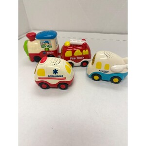 May include: Four colorful toy vehicles: a train, fire truck, ambulance, and airplane. The train is red, white, blue, and green. The fire truck is red with a yellow ladder. The ambulance is white with red accents. The airplane is white and blue.