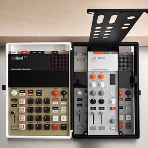 Op de afbeelding: Een wit en zwart elektronische muziek sampler en sequencer met een goudkleurig bedieningspaneel met zwarte knoppen gelabeld A, B, C en D, en een grijs paneel gelabeld K.O. II en K.O. SIDEKICK met oranje en witte draaiknoppen en schuifregelaars.