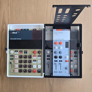 May include: A dual-unit electronic music sampler and mixer set. The left unit is white with a gold faceplate, labeled Medieval, featuring a grid of buttons and a speaker. The right unit is black with a light gray faceplate, labeled K.O. II.