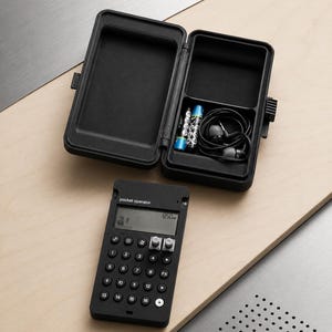 Pode incluir: Um sintetizador pocket operator preto com visor digital e botões numerados, acompanhado por um estojo de armazenamento preto aberto contendo duas pilhas e auriculares pretos com fio. O dispositivo apresenta o texto pocket operator.