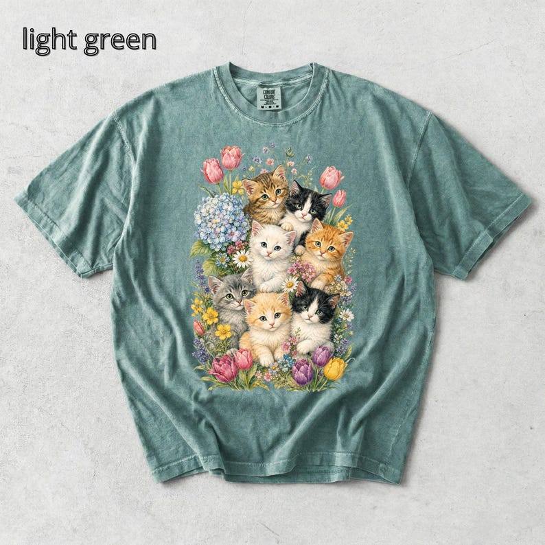 Puede incluir: Camiseta verde claro con una ilustraci&oacute;n floral de gatitos. El texto "light green" est&aacute; incluido. La camiseta tiene cuello redondo y mangas cortas. El dise&ntilde;o presenta varias flores y varios gatitos.