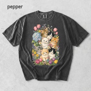 Puede incluir: Camiseta gris oscuro con una colorida ilustraci&oacute;n de gatitos y flores. Los gatitos tienen varios colores de pelaje, incluyendo naranja, gris y blanco. La palabra "pepper" est&aacute; impresa en la esquina superior izquierda.