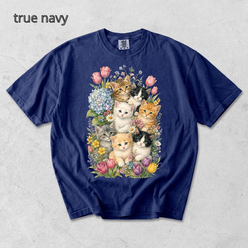 Puede incluir: Camiseta azul marino con una ilustraci&oacute;n de acuarela de gatitos y flores. Los gatitos son de varios colores, incluyendo naranja, gris y blanco. El texto "true navy" est&aacute; en la parte superior izquierda.
