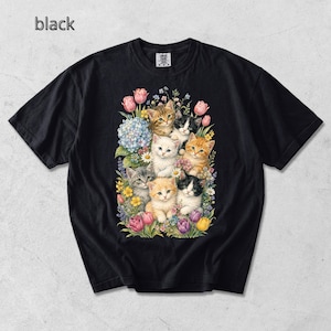 Puede incluir: Camiseta negra con una colorida ilustraci&oacute;n de gatitos rodeados de flores. Los gatitos tienen varios colores de pelaje, incluyendo blanco, naranja, gris y blanco y negro. La palabra "black" est&aacute; impresa en la esquina superior izquierda.
