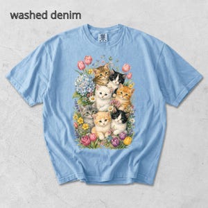 Puede incluir: Camiseta azul claro con un gr&aacute;fico de varios gatitos rodeados de flores. El texto "washed denim" est&aacute; impreso en la parte superior izquierda de la camiseta. La camiseta tiene mangas cortas y cuello redondo.