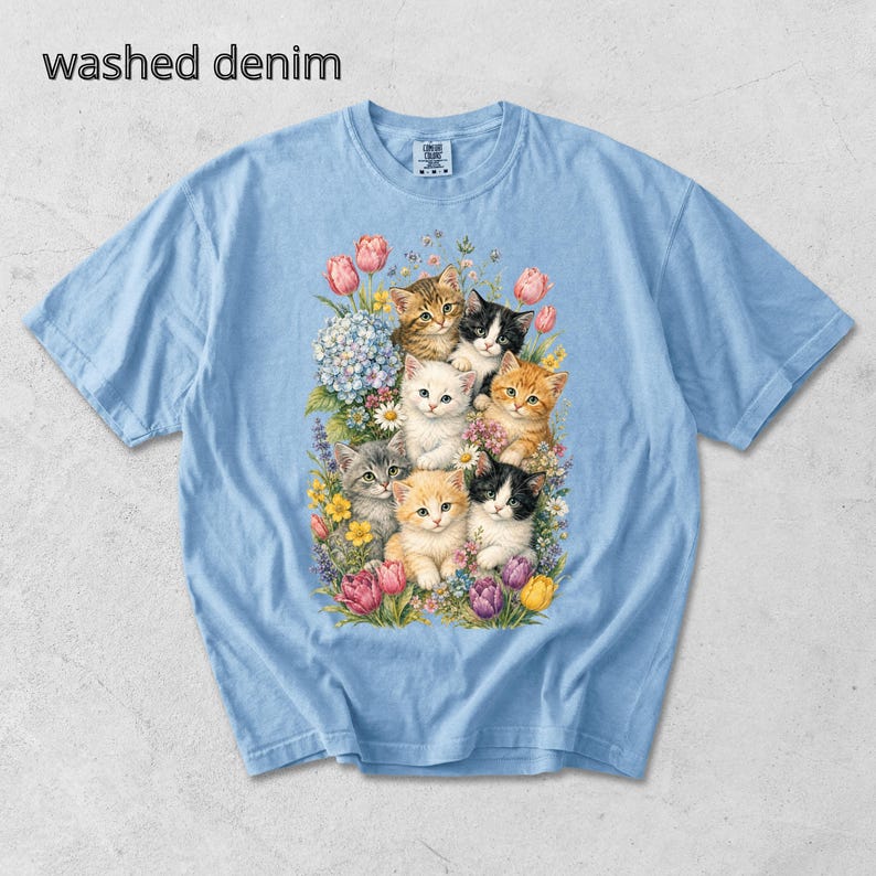 Puede incluir: Camiseta azul claro con un gr&aacute;fico de varios gatitos rodeados de flores. El texto "washed denim" est&aacute; impreso en la parte superior izquierda de la camiseta. La camiseta tiene mangas cortas y cuello redondo.