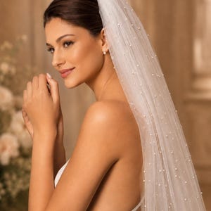 Puede incluir: Un velo de novia blanco y transparente con peque&ntilde;as perlas blancas dispersas por toda la tela. El velo est&aacute; sujeto en la parte superior y cae hacia abajo, creando una apariencia suave y superpuesta con una textura delicada y est&eacute;tica cl&aacute;sica.