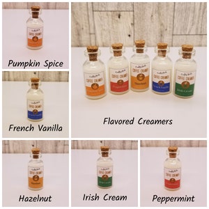 May include: A set of ten small glass bottles with cork tops, each filled with a white liquid and labeled with different coffee creamer flavors: Pumpkin Spice, Peppermint, Hazelnut, French Vanilla, and Irish Cream. The bottles are arranged in a grid pattern on a wooden surface.