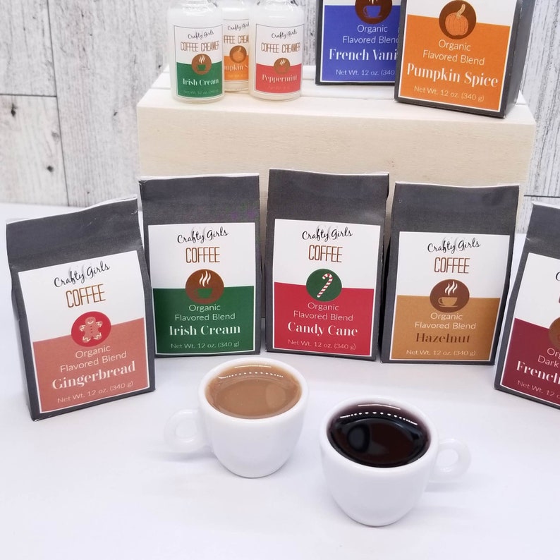 May include: Six small bags of organic flavored coffee blends with labels that include the flavors: Gingerbread, Irish Cream, Candy Cane, Hazelnut, French Vanilla, and Pumpkin Spice. The bags are arranged in a row on a wooden surface. Two small white coffee cups with coffee inside are in the foreground.