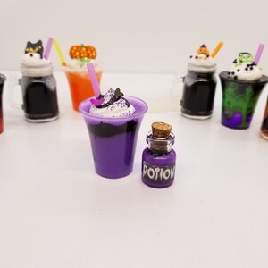 May include: A purple and black Halloween-themed milkshake with whipped cream and sprinkles, served in a clear plastic cup with a pink straw. A small glass bottle with a cork stopper filled with purple liquid and a label that reads "POTION" is next to the milkshake.