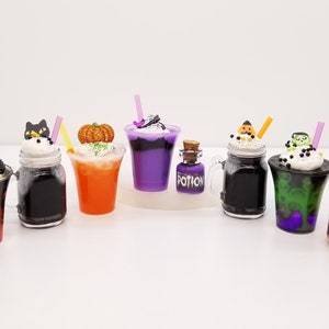 May include: Eight Halloween-themed drinks in various glass containers with black and white whipped cream, colourful toppings, and straws. The drinks include a pumpkin, a ghost, a bat, a cat, a witch, a monster, and a potion bottle.