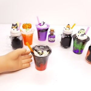 May include: A set of seven miniature Halloween-themed drinks in clear glass jars and cups with black, orange, purple, and green liquids. The drinks are topped with whipped cream and various Halloween-themed decorations, including a black cat, a pumpkin, a ghost, a monster, and a bat. A small bottle labelled "Potion" is also included.