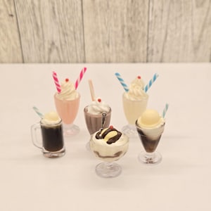May include: Miniature desserts including milkshakes, sundaes, and a root beer float. The milkshakes are pink, white, and yellow, with striped straws. The sundaes have chocolate and vanilla ice cream. The root beer float has a scoop of ice cream.