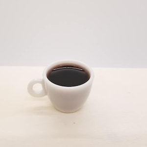 May include: A white ceramic coffee cup with a black coffee inside. The cup has a rounded handle.