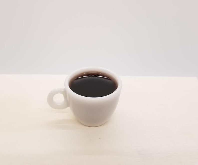 May include: A white ceramic coffee cup with a black coffee inside. The cup has a rounded handle.