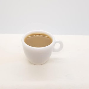 May include: A white ceramic coffee mug filled with light brown coffee.
