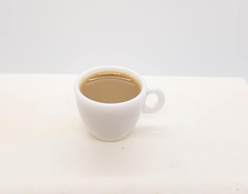 May include: A white ceramic coffee mug filled with light brown coffee.