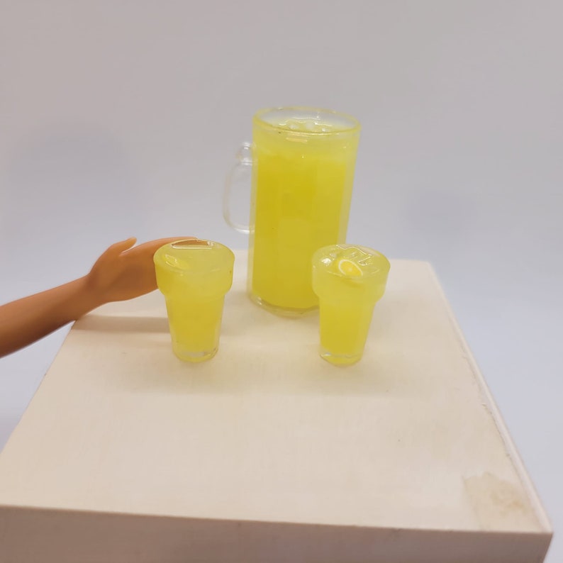 May include: A yellow pitcher and two glasses filled with lemonade. The pitcher has a handle and the glasses have a lemon slice in them.