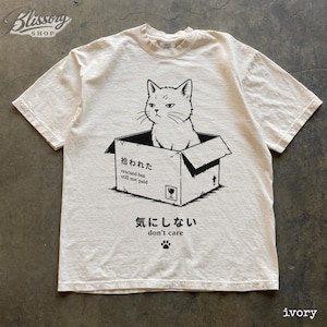 K&ouml;nnte beinhalten: Ein elfenbeinfarbenes Kurzarm-T-Shirt mit einer schwarzen Grafik einer Katze, die in einem Pappkarton sitzt. Der Karton tr&auml;gt den Text "拾われた rescued but still not paid" und das T-Shirt enth&auml;lt den Text "気にしない don't care" mit einem Pfotenabdruck.