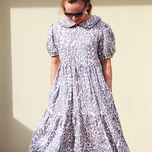 K&ouml;nnte beinhalten: Ein mehrlagiges Midikleid mit R&uuml;schenkragen und Leopardenmuster in Grau- und Wei&szlig;t&ouml;nen.