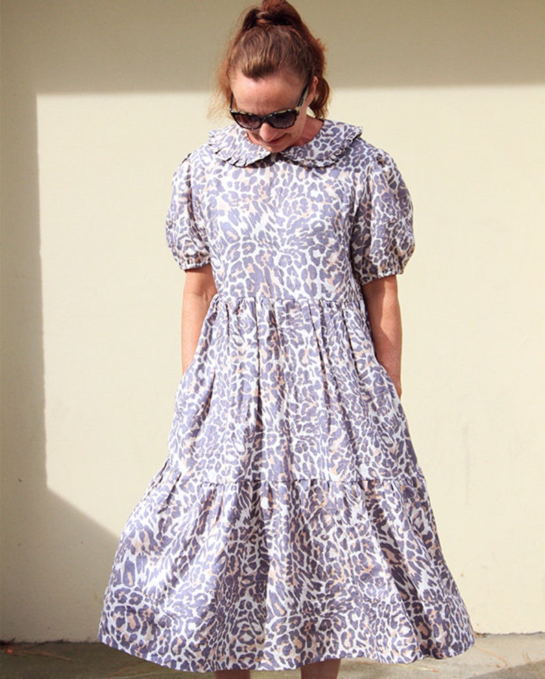 K&ouml;nnte beinhalten: Ein mehrlagiges Midikleid mit R&uuml;schenkragen und Leopardenmuster in Grau- und Wei&szlig;t&ouml;nen.