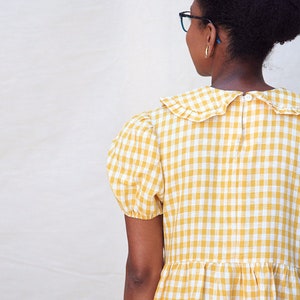 K&ouml;nnte beinhalten: Ein gelbes und wei&szlig;es Gingham-Kleid mit R&uuml;schenkragen und kurzen Puff&auml;rmeln.