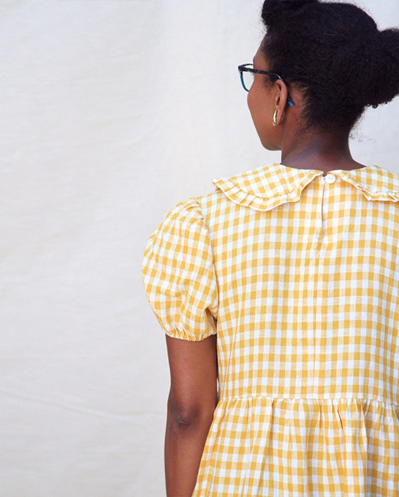 K&ouml;nnte beinhalten: Ein gelbes und wei&szlig;es Gingham-Kleid mit R&uuml;schenkragen und kurzen Puff&auml;rmeln.