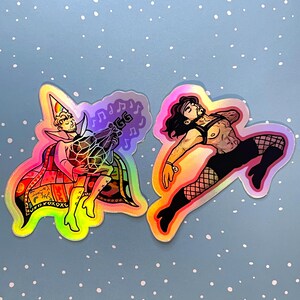 May include: Two holographic stickers featuring illustrated figures. The left sticker shows a person in a rainbow party hat and cape holding a geometric object with the letters GG. The right sticker depicts a person in a harness and fishnet stockings.