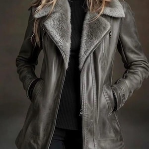 May include: Gray leather jacket with a faux fur collar. The jacket has a zipper closure, pockets, and a tailored fit. The model is wearing a black turtleneck and black pants.