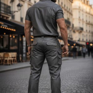 May include: A gray, short-sleeved shirt and matching cargo pants. The outfit is made of a leather-like material. The person is wearing brown boots. The background shows a European city street.