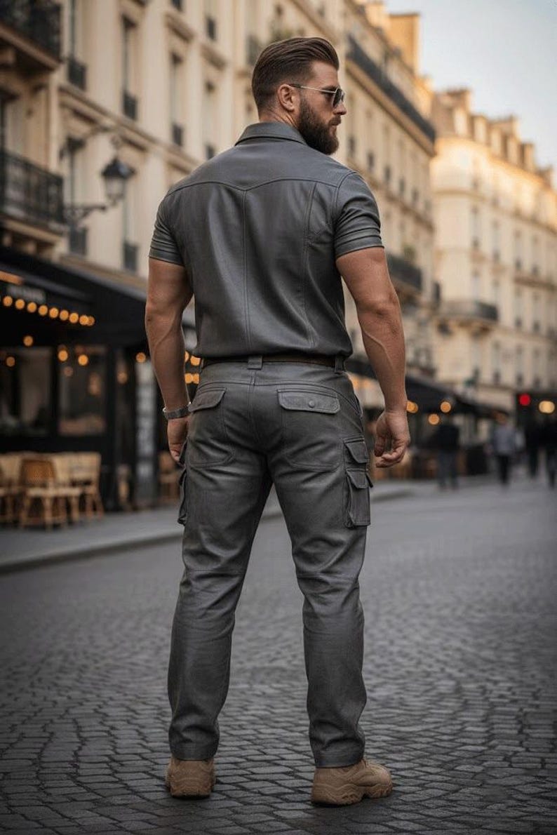May include: A gray, short-sleeved shirt and matching cargo pants. The outfit is made of a leather-like material. The person is wearing brown boots. The background shows a European city street.