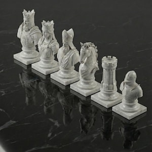 May include: A set of six white marble chess pieces, including a king, queen, bishop, knight, rook, and pawn. Each piece is a bust on a square base. The pieces are arranged in a row on a black, reflective surface.