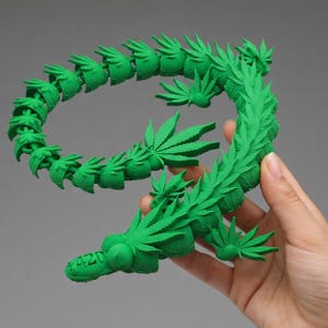 May include: A bright green, 3D-printed sculpture in the shape of the number nine, adorned with cannabis leaves. The number "420" is printed on the base of the sculpture. The sculpture is held by a hand.
