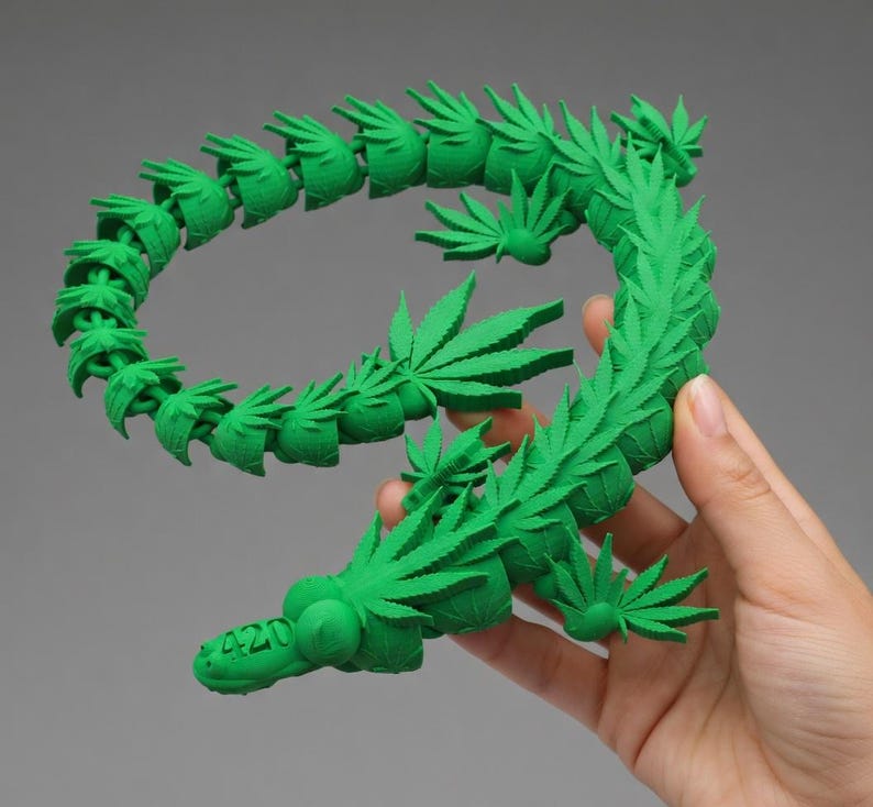 May include: A bright green, 3D-printed sculpture in the shape of the number nine, adorned with cannabis leaves. The number "420" is printed on the base of the sculpture. The sculpture is held by a hand.
