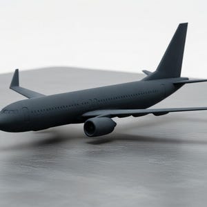 May include: A dark gray model airplane with detailed wings, tail, and engine. The miniature aircraft is set against a neutral background, showcasing its design. The model is a representation of a commercial airliner.