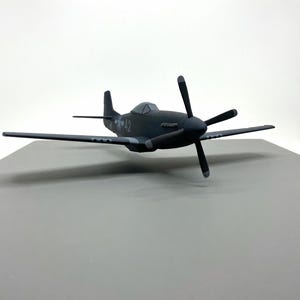 May include: A dark gray model airplane with a four-blade propeller. The plane has a streamlined design with wings and a tail. The number "42" is visible on the side of the plane. The model is set against a neutral background.