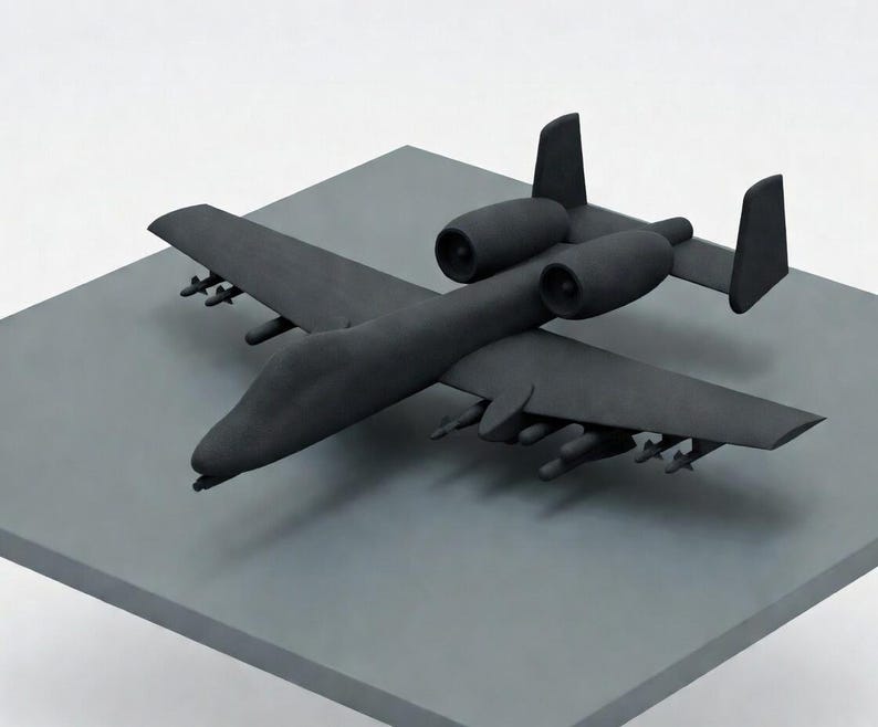 May include: A matte black model airplane with two engines and missiles under the wings. The aircraft is positioned on a gray square surface, set against a white background. The model has a detailed design.